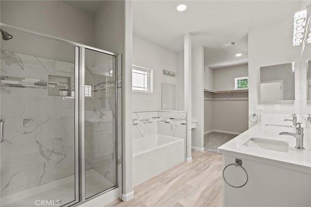 full bath with a wealth of natural light, a garden tub, a marble finish shower, and a sink