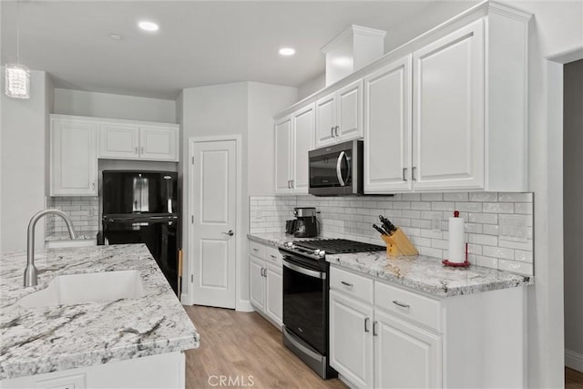 kitchen with white cabinets, stainless steel appliances, a sink, and light wood-type flooring