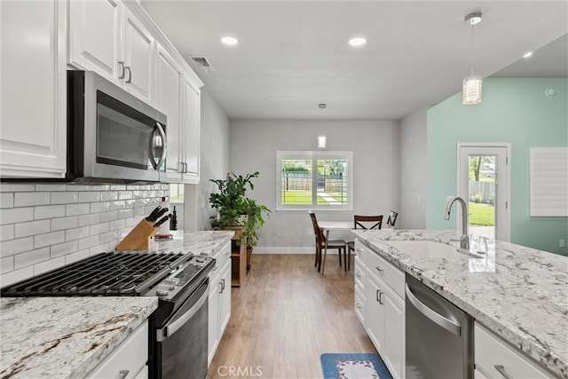 kitchen with a sink, decorative backsplash, stainless steel appliances, light wood-style flooring, and visible vents