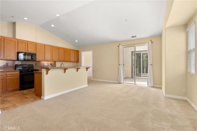 kitchen with lofted ceiling, a breakfast bar, visible vents, black appliances, and light colored carpet