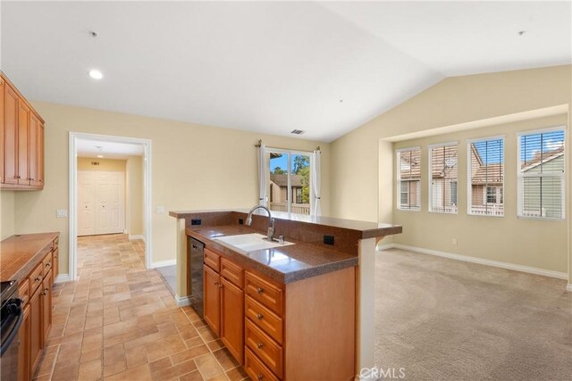 kitchen with dark countertops, dishwasher, a sink, baseboards, and a kitchen island with sink