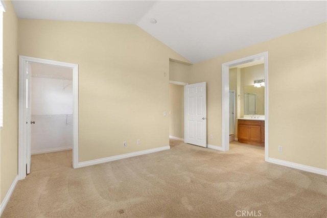 unfurnished bedroom featuring light carpet, vaulted ceiling, baseboards, and a spacious closet