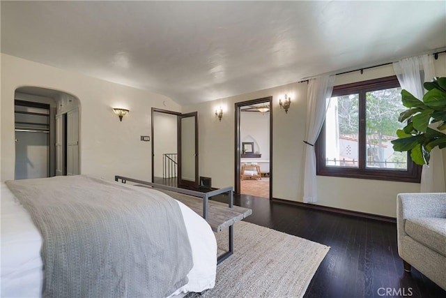 bedroom with arched walkways, wood finished floors, and baseboards