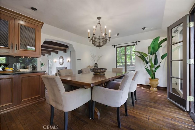 dining space with dark wood-type flooring, arched walkways, baseboards, and a notable chandelier