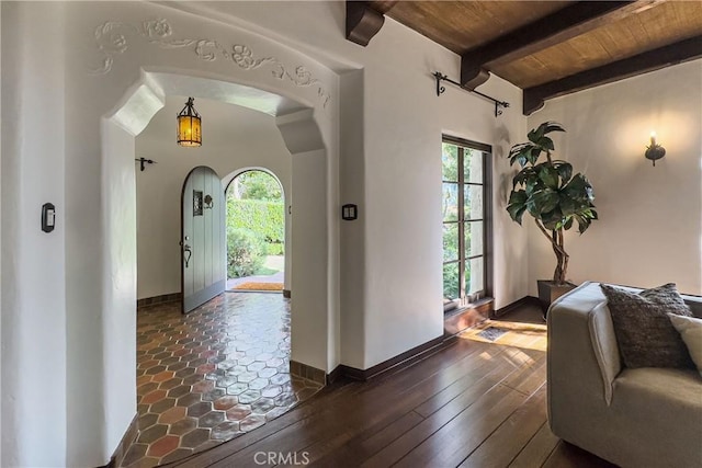 entrance foyer featuring wood ceiling, arched walkways, beamed ceiling, and baseboards