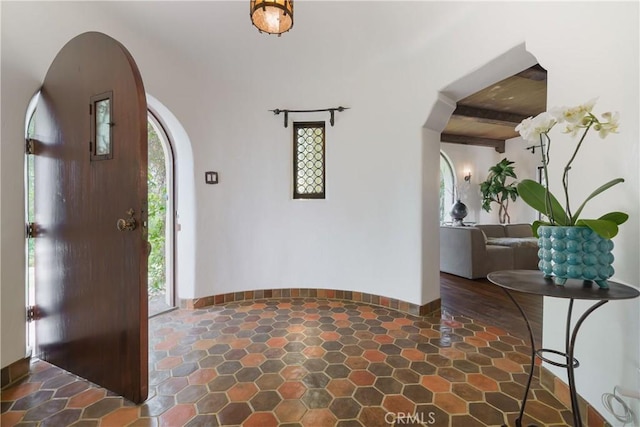 foyer entrance featuring stone finish flooring, arched walkways, and beamed ceiling