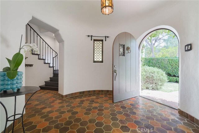 foyer with arched walkways, stairway, stone finish flooring, and baseboards