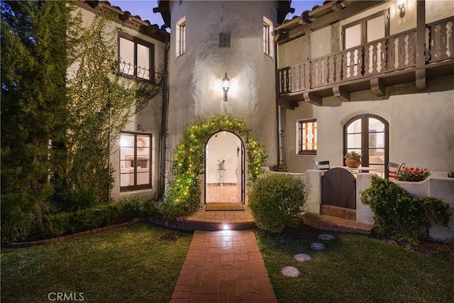 entrance to property featuring stucco siding, a lawn, and a balcony