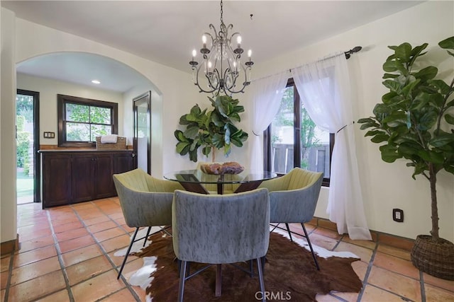 dining area with arched walkways, a notable chandelier, light tile patterned floors, and a healthy amount of sunlight