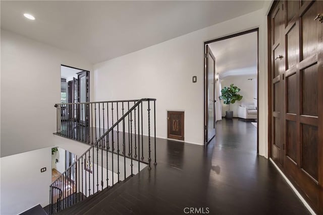 hall with wood finished floors, an upstairs landing, and recessed lighting