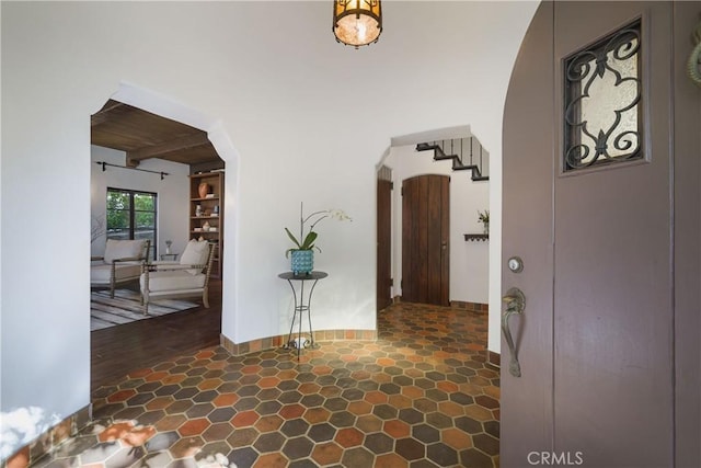 foyer entrance featuring baseboards, beam ceiling, wooden ceiling, and arched walkways