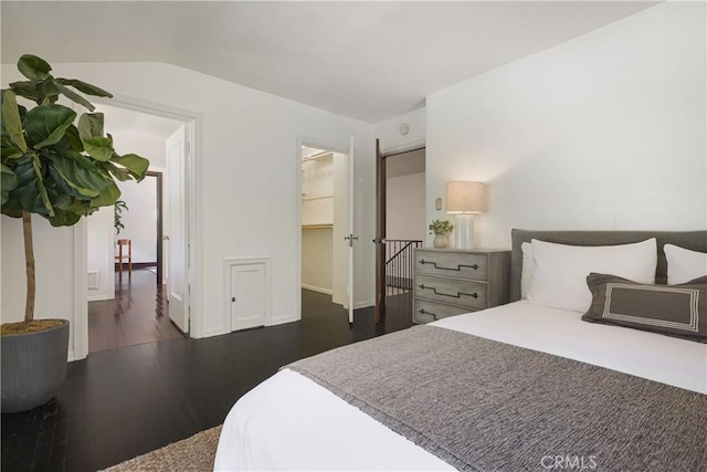 bedroom featuring a walk in closet, lofted ceiling, wood finished floors, and baseboards