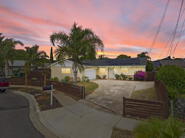 view of front of home with solar panels, a garage, a fenced front yard, and concrete driveway
