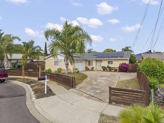 single story home featuring a garage, roof mounted solar panels, a fenced front yard, and concrete driveway