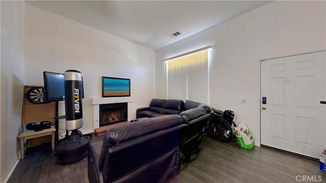 living room featuring baseboards, a fireplace with raised hearth, wood finished floors, and visible vents