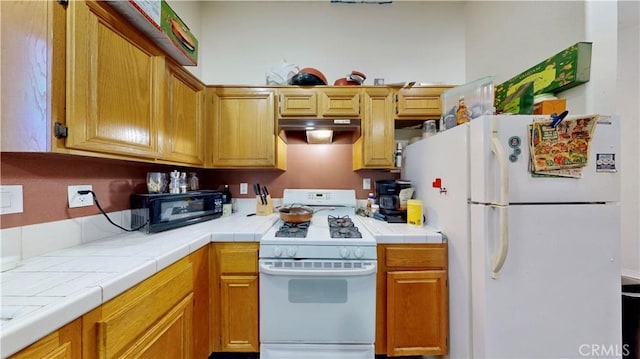 kitchen featuring white appliances, tile countertops, and under cabinet range hood
