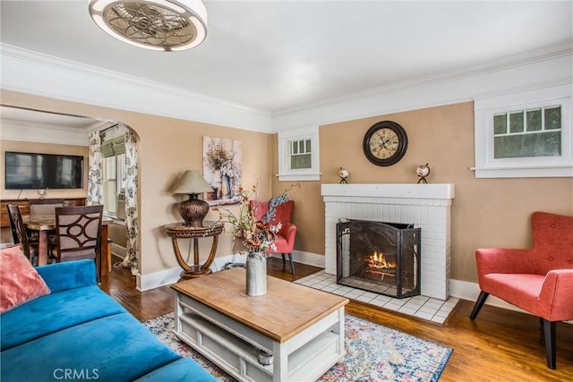 living room with ornamental molding, wood finished floors, a fireplace, baseboards, and arched walkways
