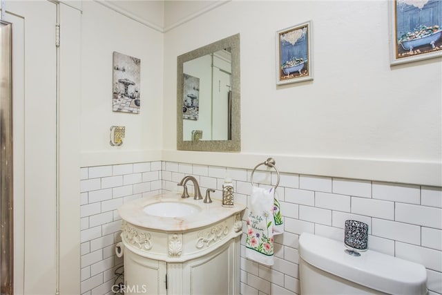 bathroom with toilet, tile walls, a wainscoted wall, and vanity