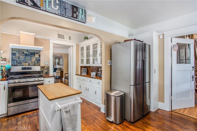 kitchen featuring appliances with stainless steel finishes, white cabinets, arched walkways, and wood counters
