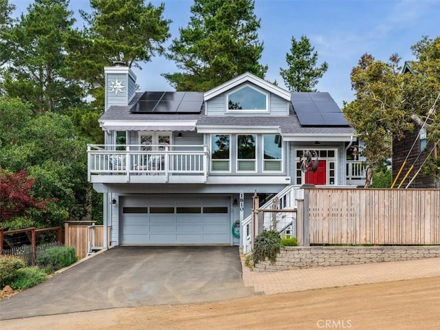 view of front facade with roof mounted solar panels, an attached garage, a chimney, and driveway