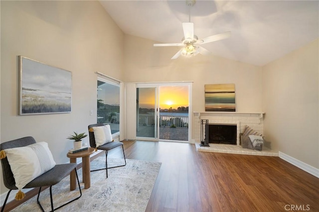 sitting room with vaulted ceiling, a ceiling fan, wood finished floors, baseboards, and a brick fireplace