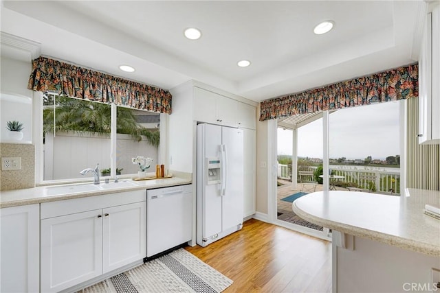 kitchen featuring light wood-style floors, white cabinetry, a sink, and white appliances