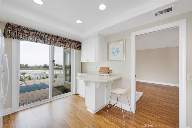 kitchen with light wood-type flooring, baseboards, a breakfast bar, and visible vents