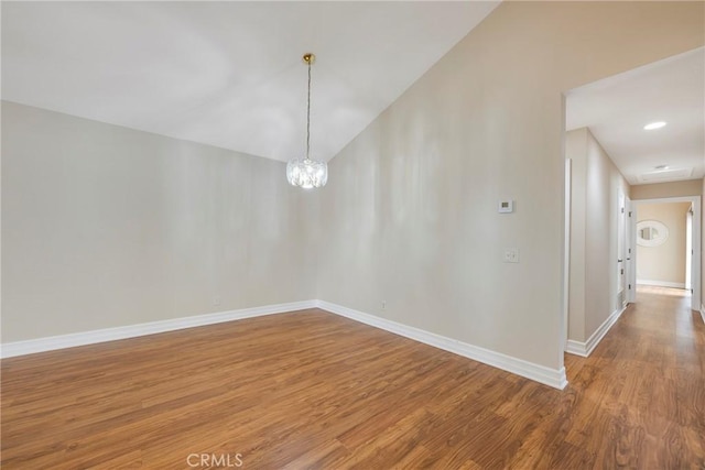 empty room with baseboards, vaulted ceiling, wood finished floors, and an inviting chandelier