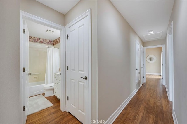 corridor with attic access, baseboards, wood finished floors, and visible vents