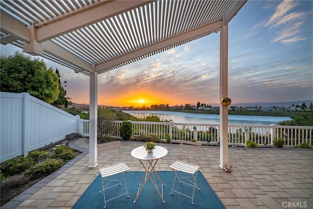 patio terrace at dusk featuring fence and a water view