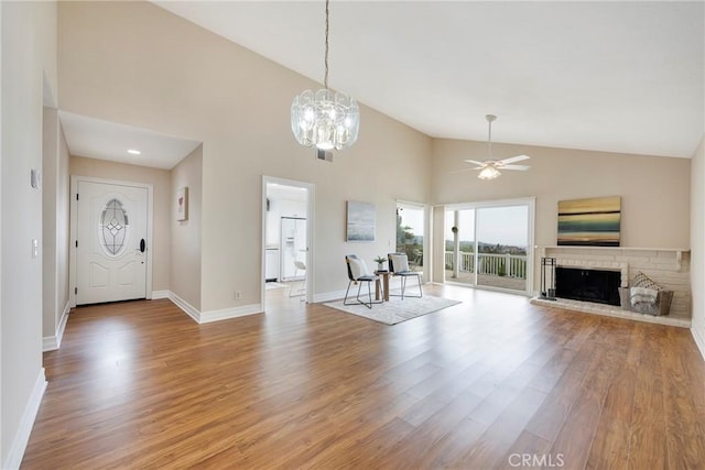 unfurnished living room featuring a fireplace with raised hearth, light wood-style floors, baseboards, high vaulted ceiling, and ceiling fan with notable chandelier
