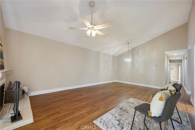 living room featuring ceiling fan with notable chandelier, baseboards, wood finished floors, and a fireplace