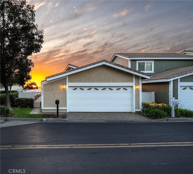 view of front of property featuring a garage, driveway, stucco siding, and fence