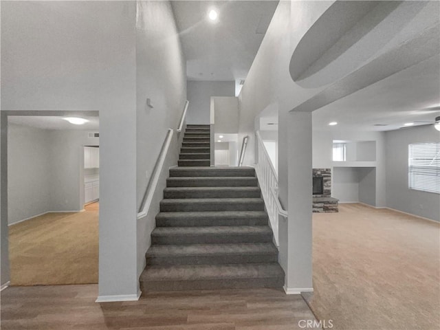 stairs with a towering ceiling, ceiling fan, carpet, and baseboards