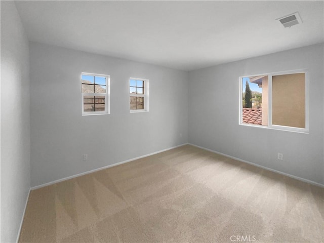 unfurnished room with light colored carpet, a healthy amount of sunlight, visible vents, and baseboards