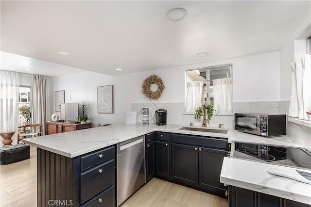 kitchen with stainless steel dishwasher, light wood finished floors, a peninsula, and light stone countertops