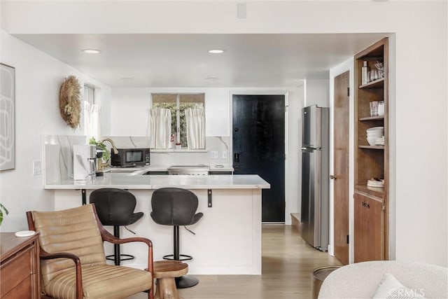 kitchen with a kitchen bar, light countertops, freestanding refrigerator, a peninsula, and light wood-style flooring
