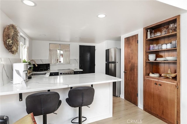 kitchen featuring freestanding refrigerator, a peninsula, light stone countertops, and a sink