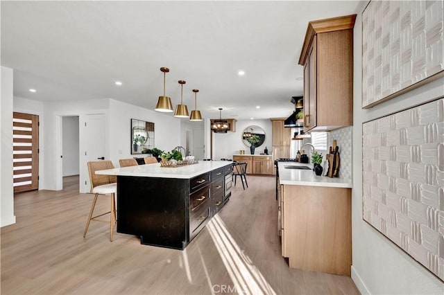 kitchen featuring light wood finished floors, a kitchen breakfast bar, a sink, light countertops, and a kitchen island