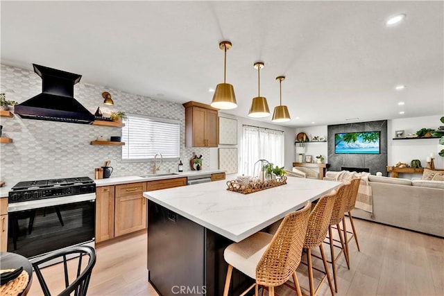 kitchen with a sink, light wood-type flooring, gas range, backsplash, and wall chimney exhaust hood
