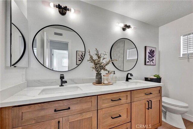 bathroom with toilet, a sink, and double vanity
