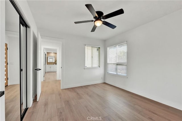 unfurnished bedroom with light wood-style flooring, a closet, a ceiling fan, and baseboards
