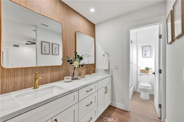 full bath featuring wood finished floors, a sink, double vanity, and toilet