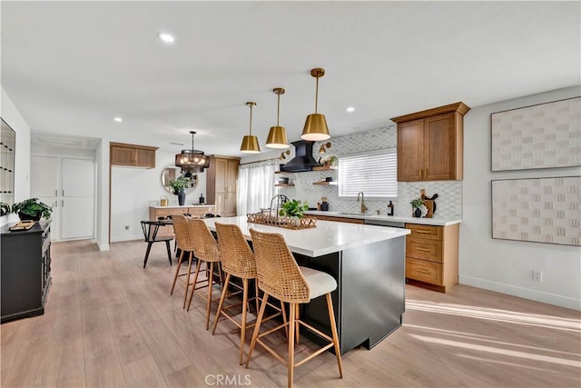kitchen with brown cabinets, light wood finished floors, backsplash, light countertops, and wall chimney range hood