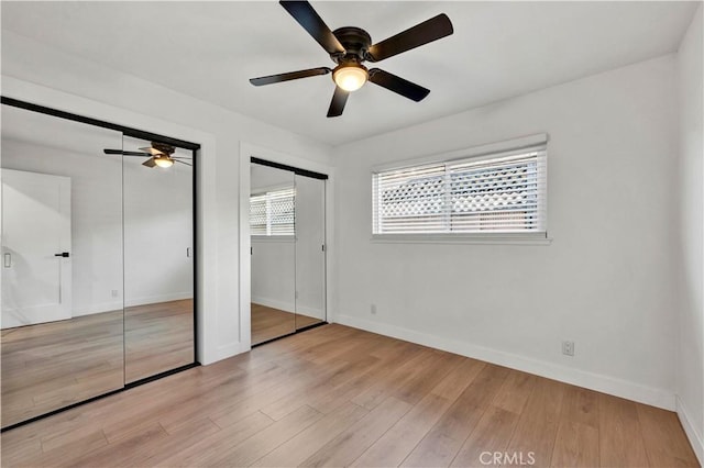 unfurnished bedroom featuring two closets, ceiling fan, baseboards, and wood finished floors