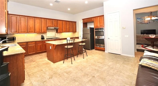 23801 Hollingsworth Dr, Murrieta, CA 92562 - kitchen with light stone counters, stainless steel appliances, a kitchen bar, under cabinet range hood, and a kitchen island