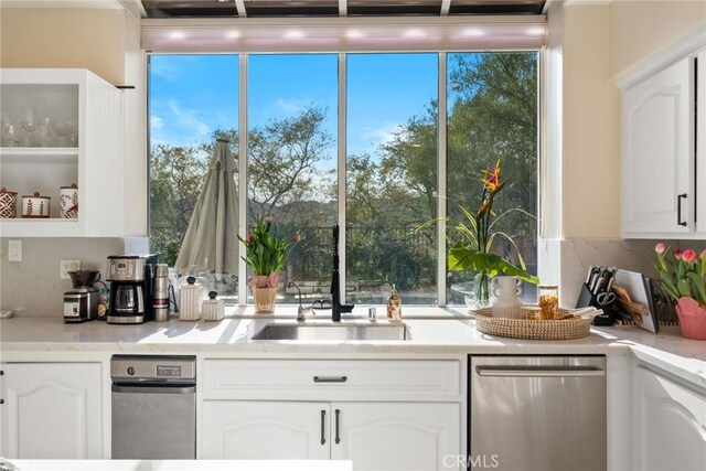 kitchen with white cabinetry, stainless steel dishwasher, a sink, light countertops, and a wealth of natural light