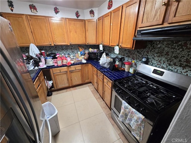 kitchen with tile counters, decorative backsplash, light tile patterned flooring, stainless steel range with gas stovetop, and under cabinet range hood