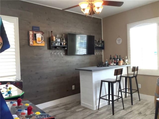 bar with baseboards, a bar, a ceiling fan, and wood finished floors