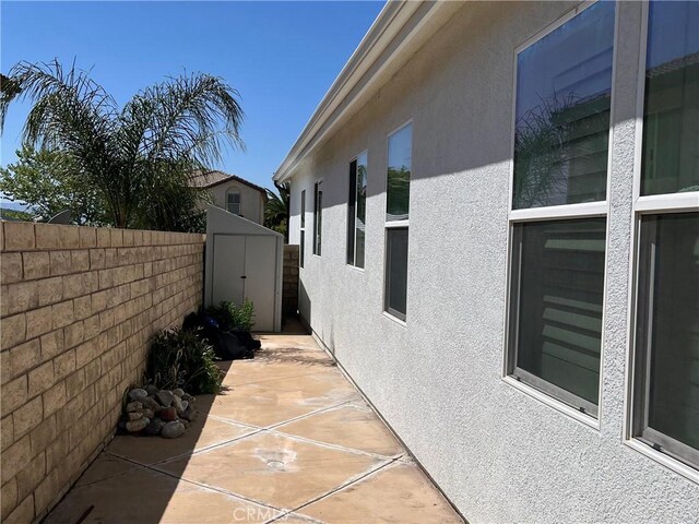 view of side of property with fence, stucco siding, a patio area, and a shed